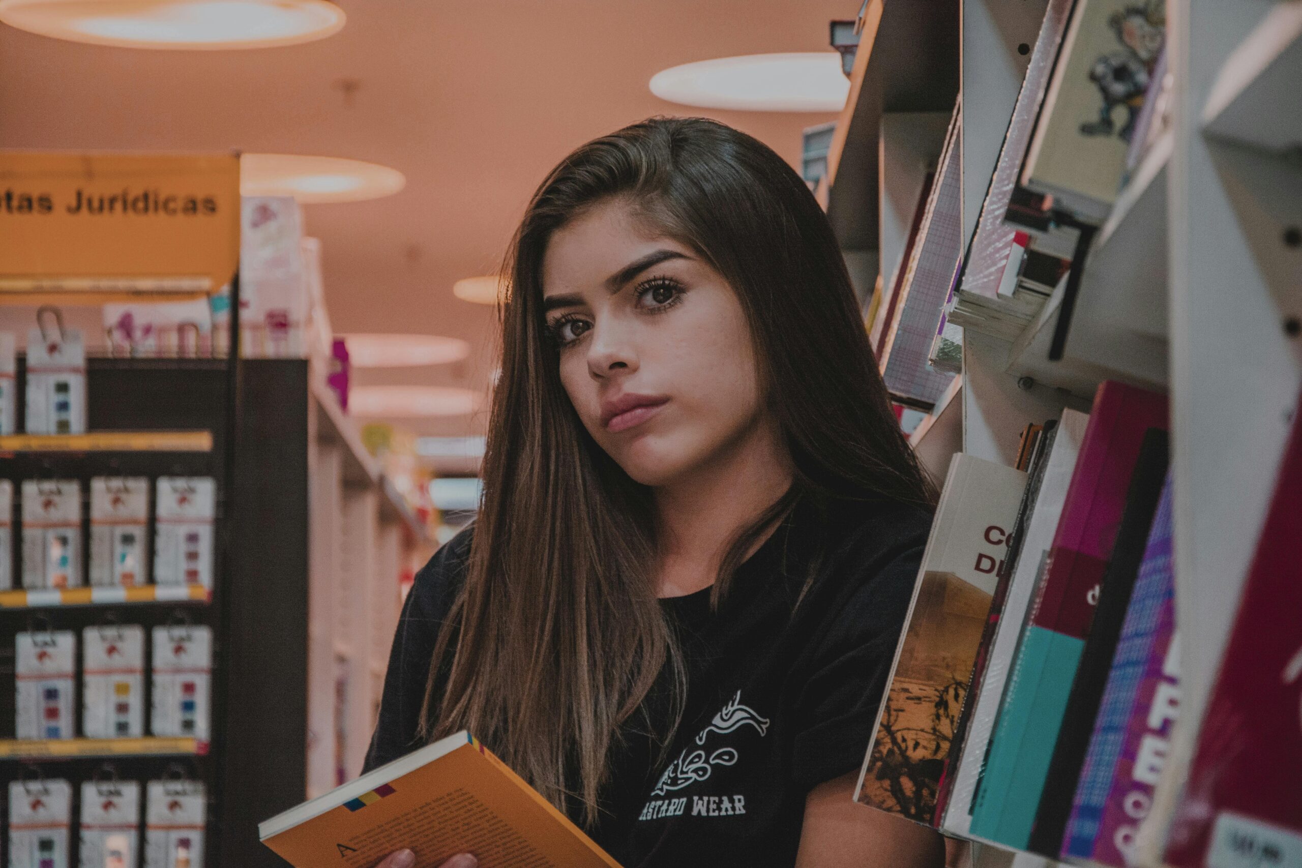 pexels-photo-2393793-2393793 A young woman with long hair reading a book in a cozy bookstore aisle.
